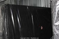 Two double-sized box springs, one with black quilted fabric cover and the other covered in beige fabric, both wrapped in protective plastic