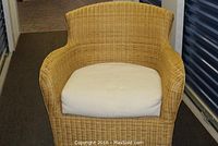 Front view of the wicker chair with beige cushion showing shape and color.