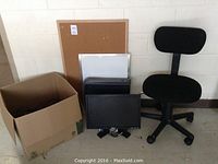Lot contents arranged showing chair, Dell monitor on stand, Dell CPU tower, black Altec Lansing speakers, multiple laptops, wired keyboard, and cardboard box with cables. A corkboard and whiteboard are in the background.