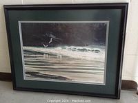 Full view of framed print leaning against wall, showing the artwork, matting, and black frame.