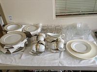 Overall display of porcelain plates, bowls, cups and saucers with gravy boat and two types of glasses.