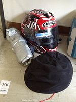 HJC red, white and black full face helmet with clear visor positioned upright with motorcycle cover folded beside it and black helmet in front