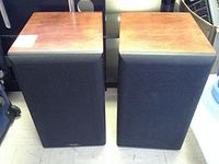 Pair of Apogee Acoustics speakers with wood finish tops and black fabric grilles covering the speakers.