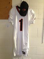 Photo of white Puma BC Lions jersey with number 1 displayed prominently and black and orange trim, hanging on a wall with a black BC Lions hat on top.