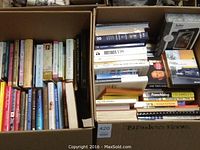 Two full boxes with assorted business and alternative books arranged vertically and stacked, along with a boxed Kobo eReader.