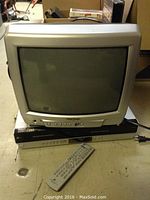 Image of a silver Insignia 14-inch CRT TV on top of a black Zenith DVD/VCR combo recorder and a remote control in front