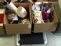 Two cardboard boxes holding assorted kitchen items including a white electric popcorn maker, plastic containers, and kitchen utensils