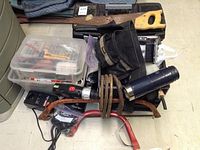 Stack of assorted tools including cordless drill, tool box, hand tools, cables, and saws.