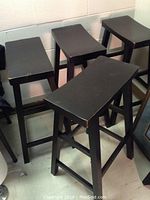 Four black wooden kitchen stools grouped together showing their design and condition.
