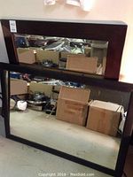 Two rectangular mirrors stacked vertically showing wooden frames and reflective surfaces with storage boxes in background.