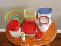 Photo of assorted Tupperware and Rubbermaid containers arranged on a wooden table, showing multiple sizes and lid colors.