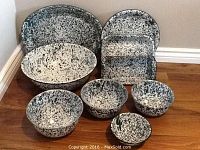 Full view of the white and green speckled enamel metal baking and serving set including an oval platter, rectangular trays, and bowls of various sizes.