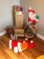 Overview of assorted Christmas decorations arranged in a corner showing tabletop tree, ornaments, wrapping paper, hats, wreath and felt Santa