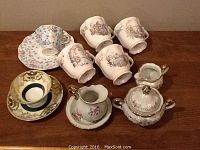 Photo of bone china cups, saucers, and small servery items arranged on wooden surface.