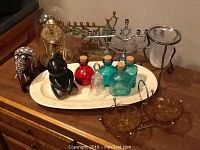 Photo of assorted decorative accessories including carved animal figurines (elephant and bear), two menorahs, bottles with cork stoppers, a dome covered clock, glass dinner bell, and amber glass candle holders arranged on a wooden surface.