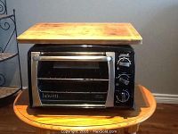 Bravetti toaster oven shown with bamboo butcher block on top. Oven is black with stainless steel front and control knobs on the side.