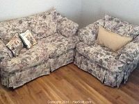 Photo of a floral upholstered loveseat and a matching lounge chair in a corner of a room on hardwood flooring, each with floral throw pillows.