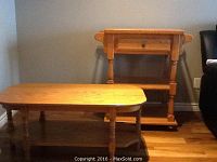Photo of an oak coffee table and a mobile multi-purpose table against a wall on a hardwood floor.
