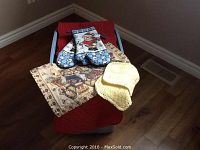 Photo showing assorted table runners, multiple placemats, and several oven mitts placed on a blue Rubbermaid storage bin on hardwood floor.