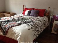 Queen size bed with cream comforter showing brown branch pattern, multiple pillows in red, white and purple, red bedskirt, woven throws on bed