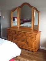Front view of oak bureau dresser with five drawers, two cabinet doors and attached three-panel mirror