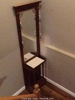 Full frontal view of tall wooden hall tree umbrella stand with mounted mirror, decorative metal hooks, and white quartz shelf near top.