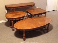 Four matching oak wood tables: oval coffee table, rectangular sofa table, round and square side tables arranged on carpeted floor against wall.