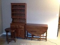 Wooden wine rack hutch, oval drop leaf table, and round side table placed side by side against a wall.
