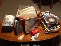 Photo showing a variety of knitting and craft pattern books stacked on the table, household iron, small box of buttons, plastic storage containers, and some small crafting accessories.