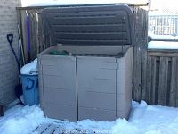 Outdoor view of tan Rubbermaid storage box against fence in winter.