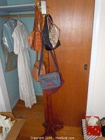 Full view of wooden hat tree holding four handbags and a white hanging dress in the background.