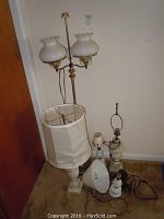Full view of all lamps in a corner showing five lamps with brass, marble, glass and fabric elements on beige carpet against white walls.