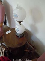 Round wooden end table with floral glass lamp on top, showing table's surface and lamp base details.
