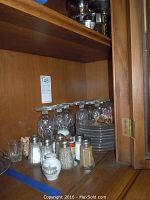 Photo showing 12 inverted clear glass dessert stemware glasses, 10 matching clear glass plates stacked, and several salt and pepper shakers on a wooden shelf.