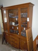 Front view of medium dark wooden hutch showing three glass-front cabinet doors on upper section and three drawers plus two side cabinets on lower section.