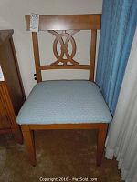 Wooden chair with padded light blue seat and decorative backrest visible, positioned near blue curtains.