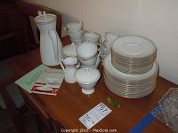 Full china set including stacked plates, teacups, teapot, sugar bowls, and creamer displayed on wooden table.