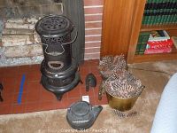 Photo of vintage Tropical black metal heater with door in front, cast iron kettle, two metal buckets filled with pine cones, and two cast irons on red tile floor.