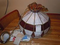 Full view of stained glass hanging light fixture on wooden table showing brass chain and mounting hardware with white and burgundy glass panels.
