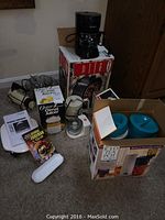 Photo showing boxed Rival oval Crock Pot, Mr. Coffee Iced Tea Pot with blue pitch lids, George Foreman Grill box, and other kitchen appliances including mixers and juicers.