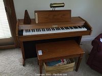 Full view of Wurlitzer electric piano 76 keys, wood case, matching bench, metronome on top, sheet music box below bench.
