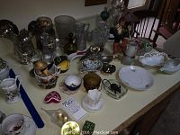 Overview of all items, showing glassware, ceramic figurines, mini oil lamps, and small collectibles.