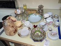 Overview of lot showing pink glass pitcher, various ceramic and china bowls, coffee cups, saucers, glassware, and jars arranged on kitchen counter.