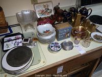 Wide view showcasing various items on countertop including Chokin art plate, blue and gold tea set, wooden decor items, glass trays, and kitchenware.