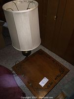 Wooden end table with decorative floral motif and surface wear, accompanied by the tall table lamp with white fabric lampshade.