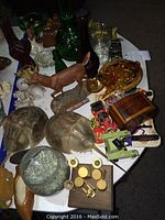 Photo of assorted knick knacks including wooden deer figurine, horseshoe crab shells, glass elements, tin toy cars, wooden carved items and porcelain doll.