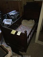 Front and side view of dark wooden antique rocking cradle showing carved details, slatted sides, and rocker base with patchwork quilt inside.