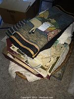 Collection of vintage linens piled in a basket including woven blankets, lace doilies, and folded fabrics.