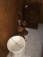 Photo showing two tall wooden lamps with inlaid wood designs and a wooden night stand with brass drawer handles against a wood-paneled wall.