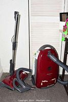 Full view of the Panasonic vacuum cleaner with hose, detachable hand vacuum and floor cleaning head, placed on carpet against a wall.